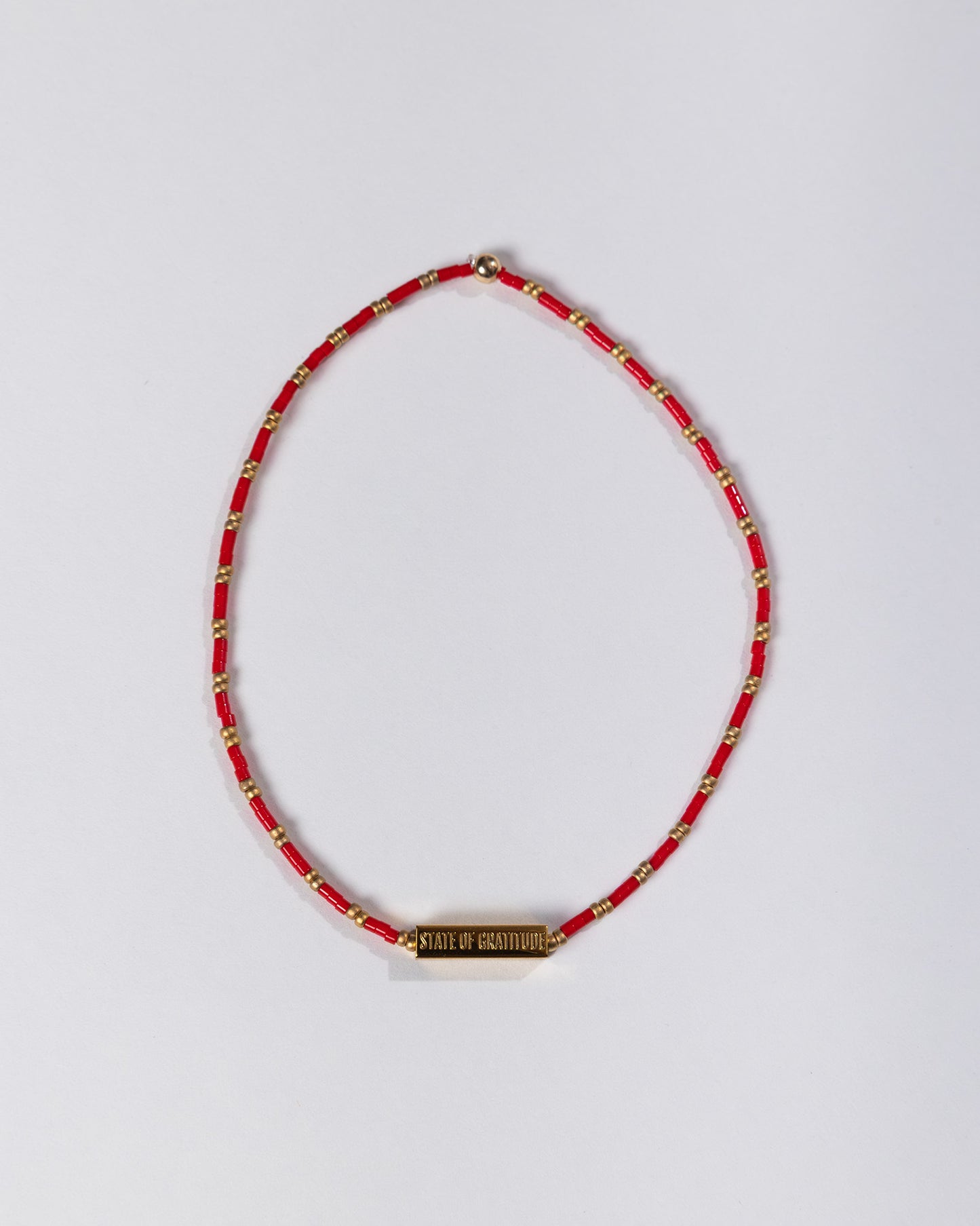 Red beaded necklace with a gold tag on a light gray background