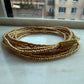 Gold beaded bracelet on a marble surface with a blurred window background