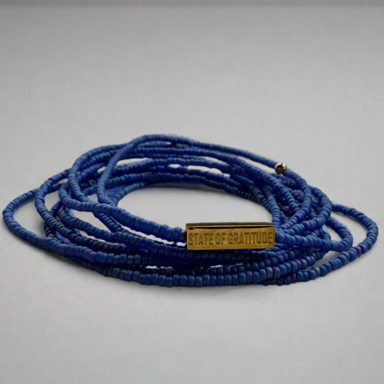 Blue beaded bracelet with a gold tag on a white background
