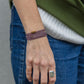 Close-up of a person's wrist wearing a bracelet and ring, with a green sweater and blue jeans.