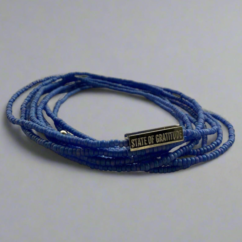 Blue beaded bracelet with a gold tag on a light gray background