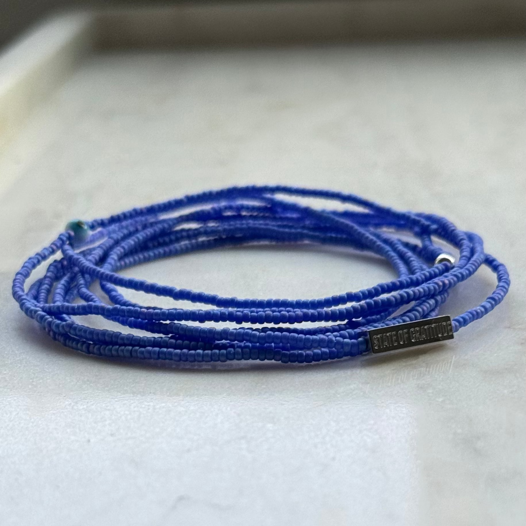 Blue beaded necklace with a metal tag on a light gray background