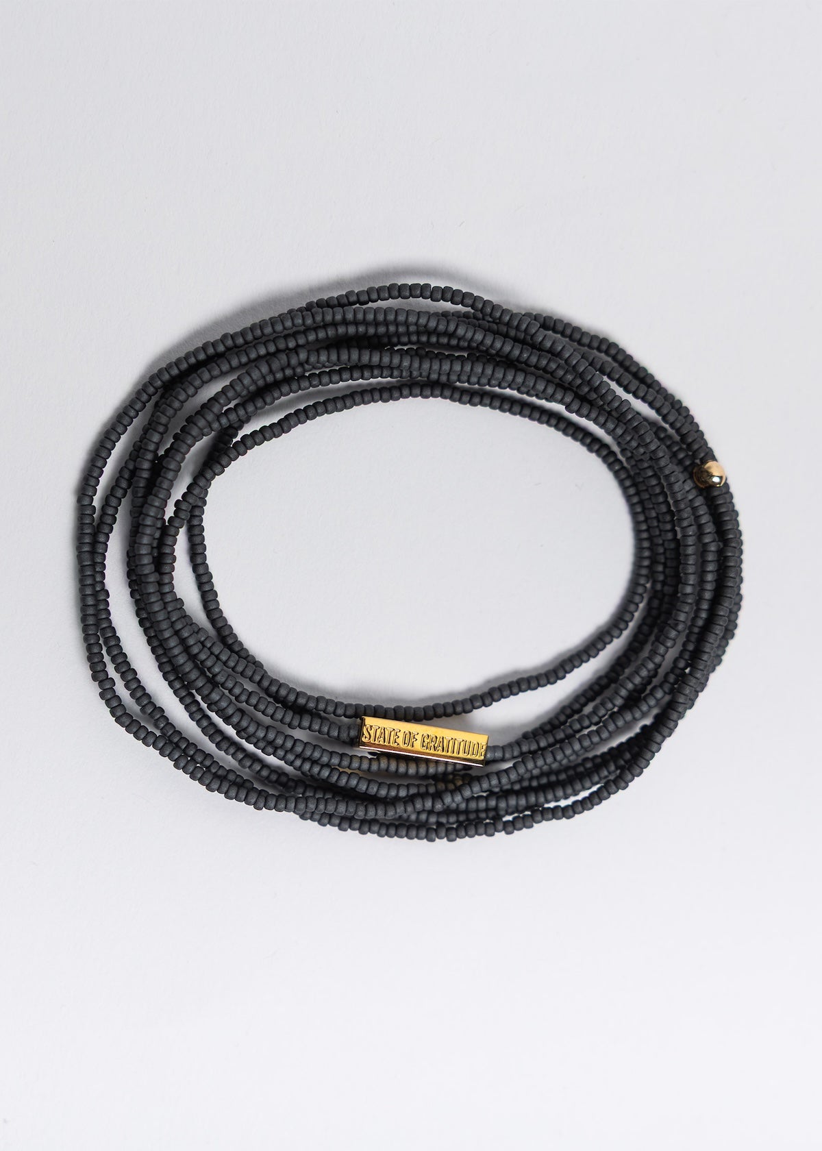 Black beaded necklace with a gold tag on a light gray background