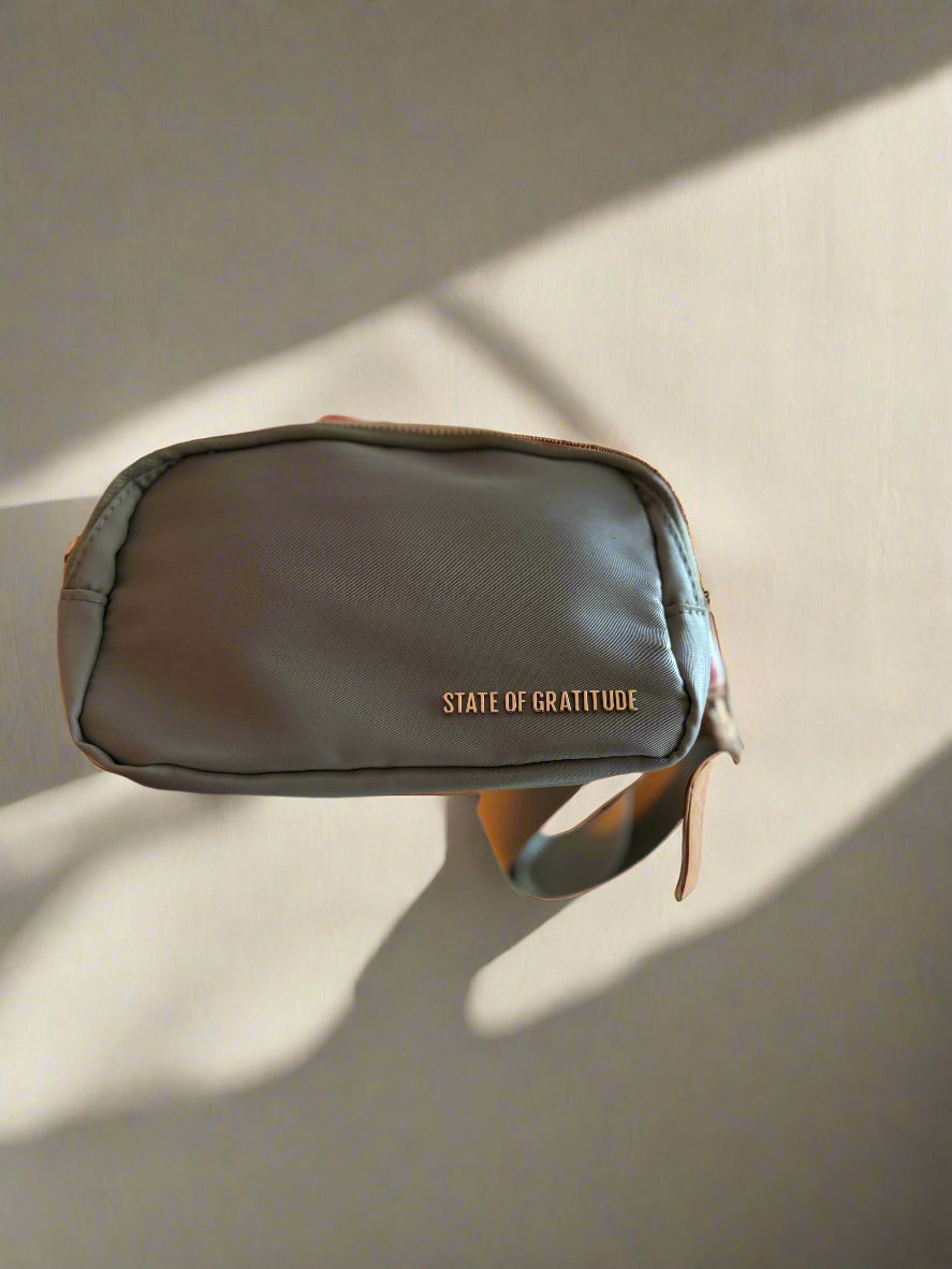 sage green belt bag with 'State of Gratitude' branding on a beige background