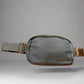 Gray waist bag with gold accents held by a hand against a light background