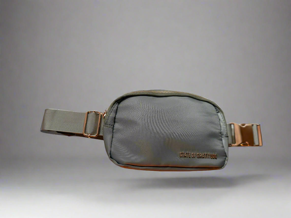 Gray waist bag with gold accents held by a hand against a light background