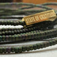 Green beaded bracelet with a gold tag labeled 'State of Gratitude' on a textured surface.