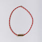 Red beaded necklace with a gold tag on a light gray background