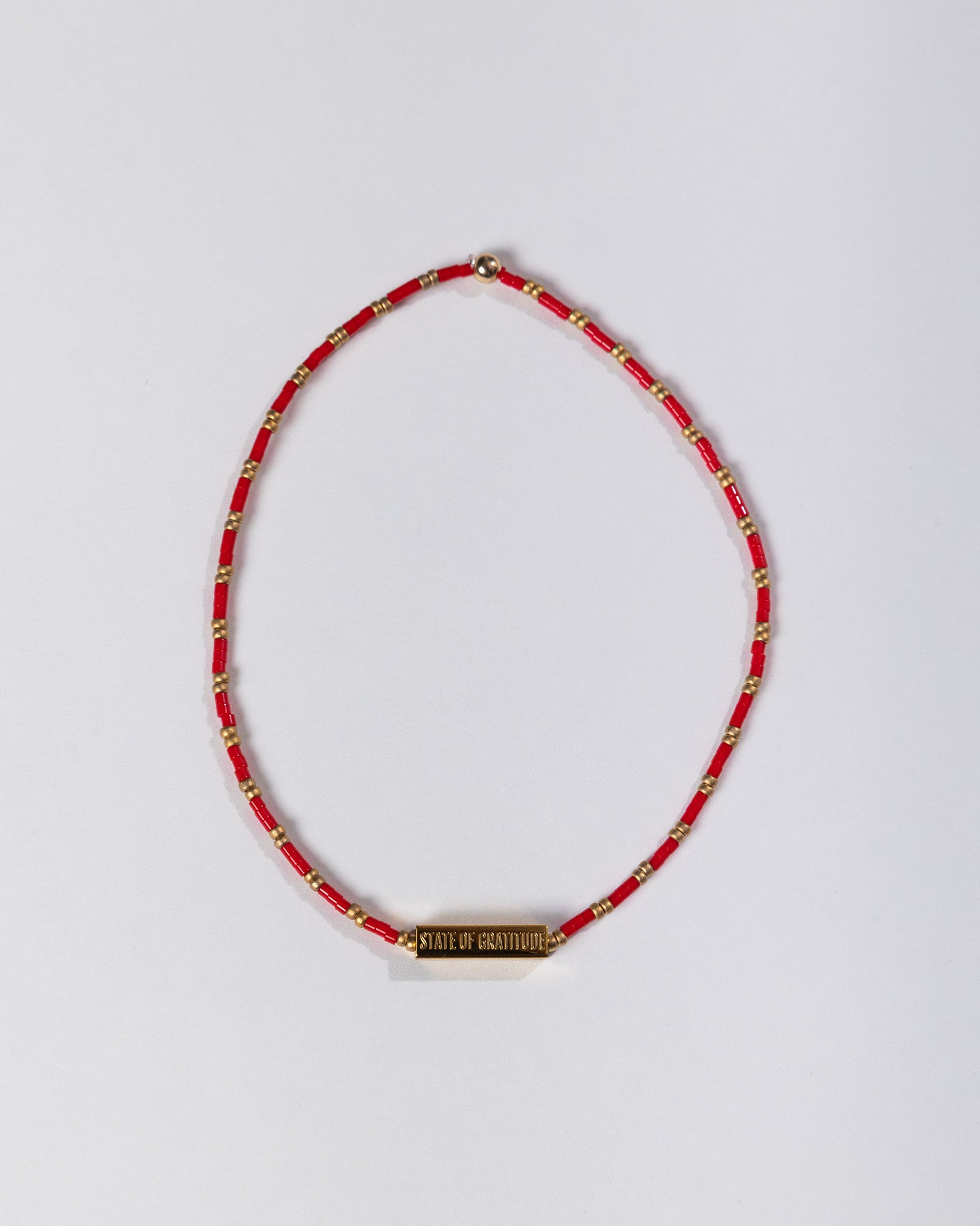 Red beaded necklace with a gold tag on a light gray background