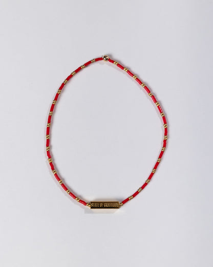 Red beaded necklace with a gold tag on a light gray background