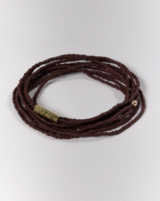 Brown beaded bracelet with a gold tag on a white background
