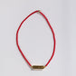 Red string bracelet with a gold bar charm on a white background