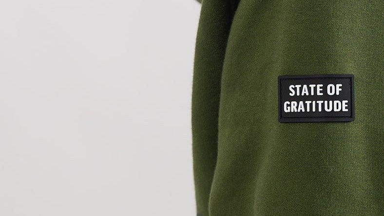 Green sweatshirt with 'STATE OF GRATITUDE' patch on a light gray background