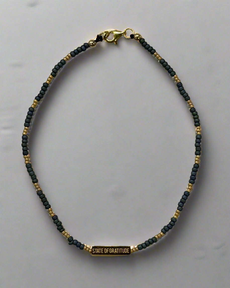 single-stranded bracelet with gold and dark blue beads on a light gray background