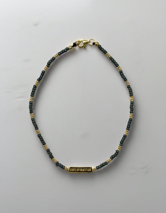 single-stranded bracelet with gold and dark blue beads on a light gray background