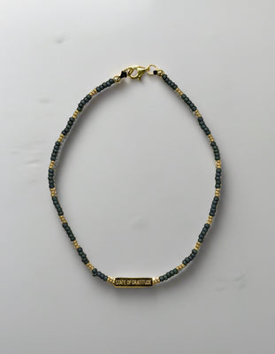 single-stranded bracelet with gold and dark blue beads on a light gray background