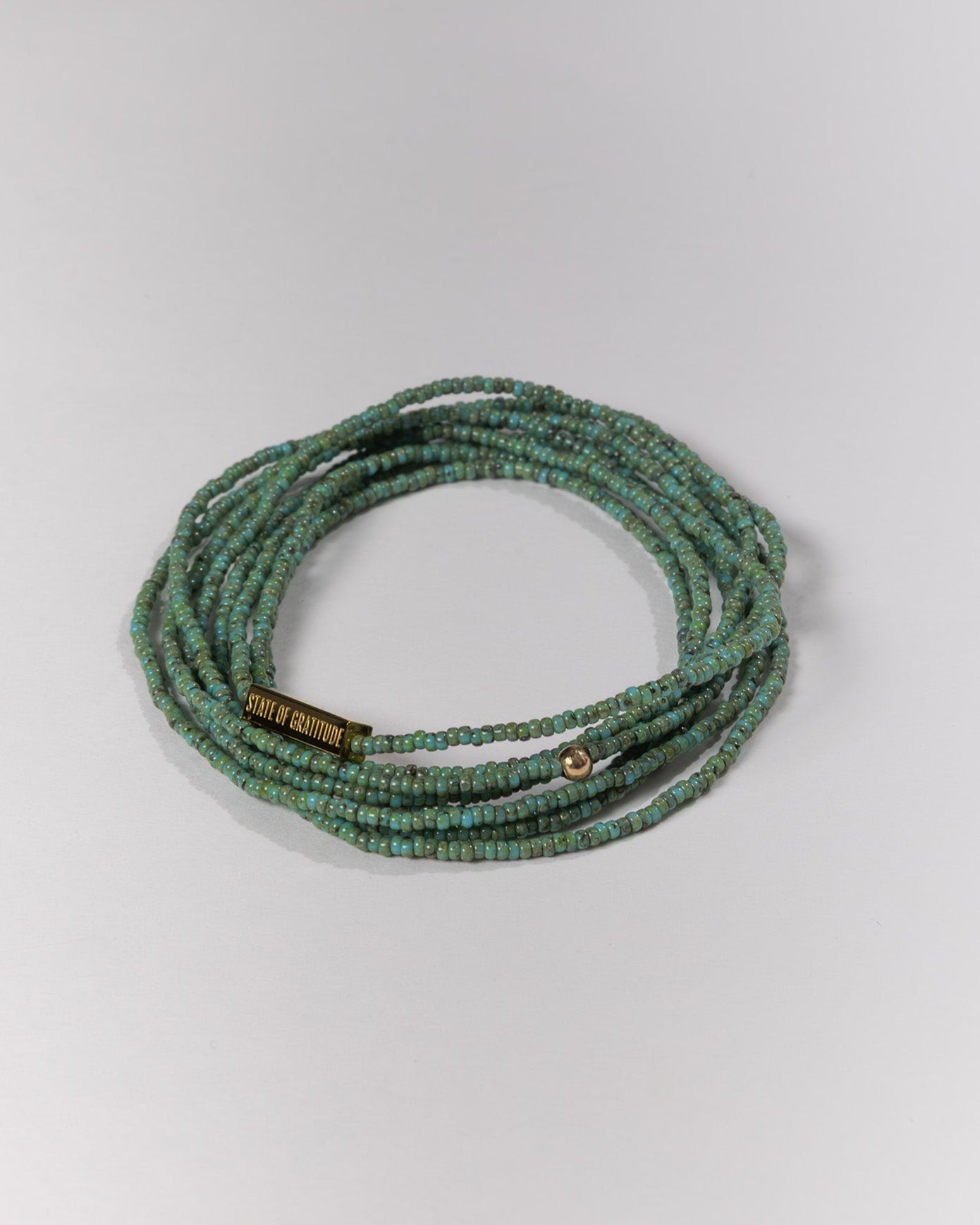Green beaded bracelet with a gold bead on a light gray background