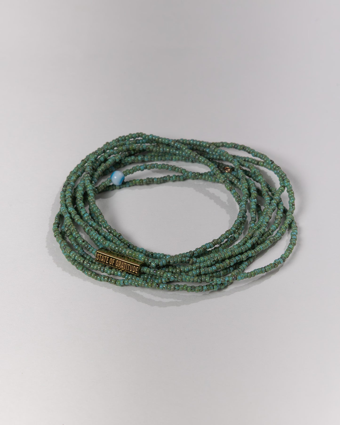Green beaded bracelet with a visible brand tag on a light gray background