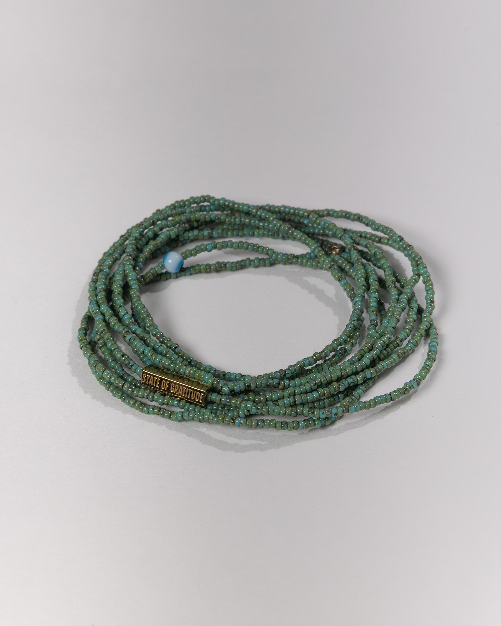 Green beaded bracelet with a visible brand tag on a light gray background