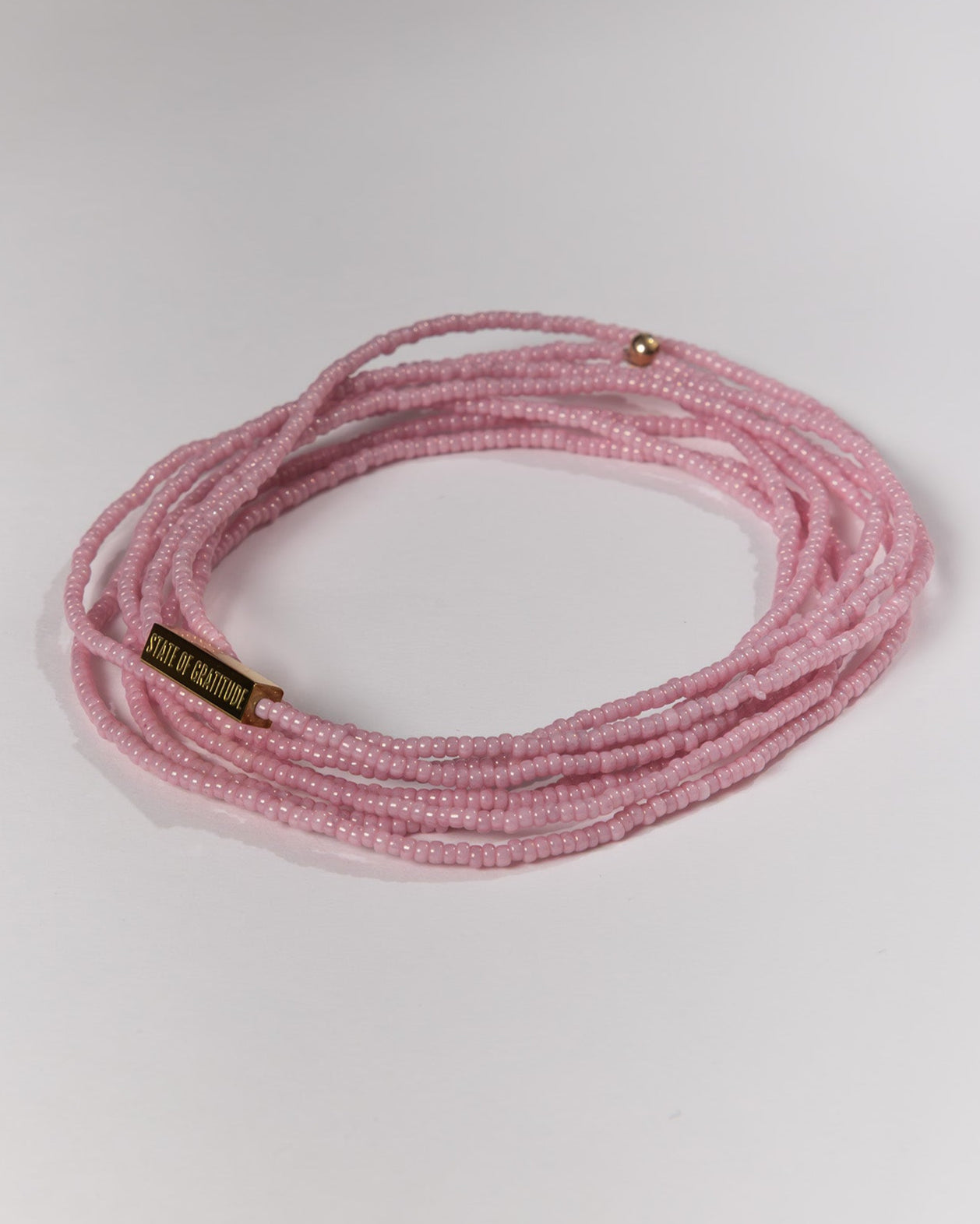 Pink beaded bracelet on a white background with gold link reading STATE OF GRATITUDE